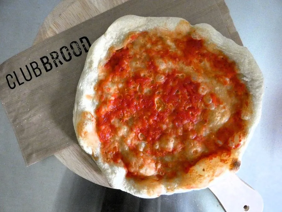Licht voorgebakken desembodem met tomatensaus op een Club Brood plank