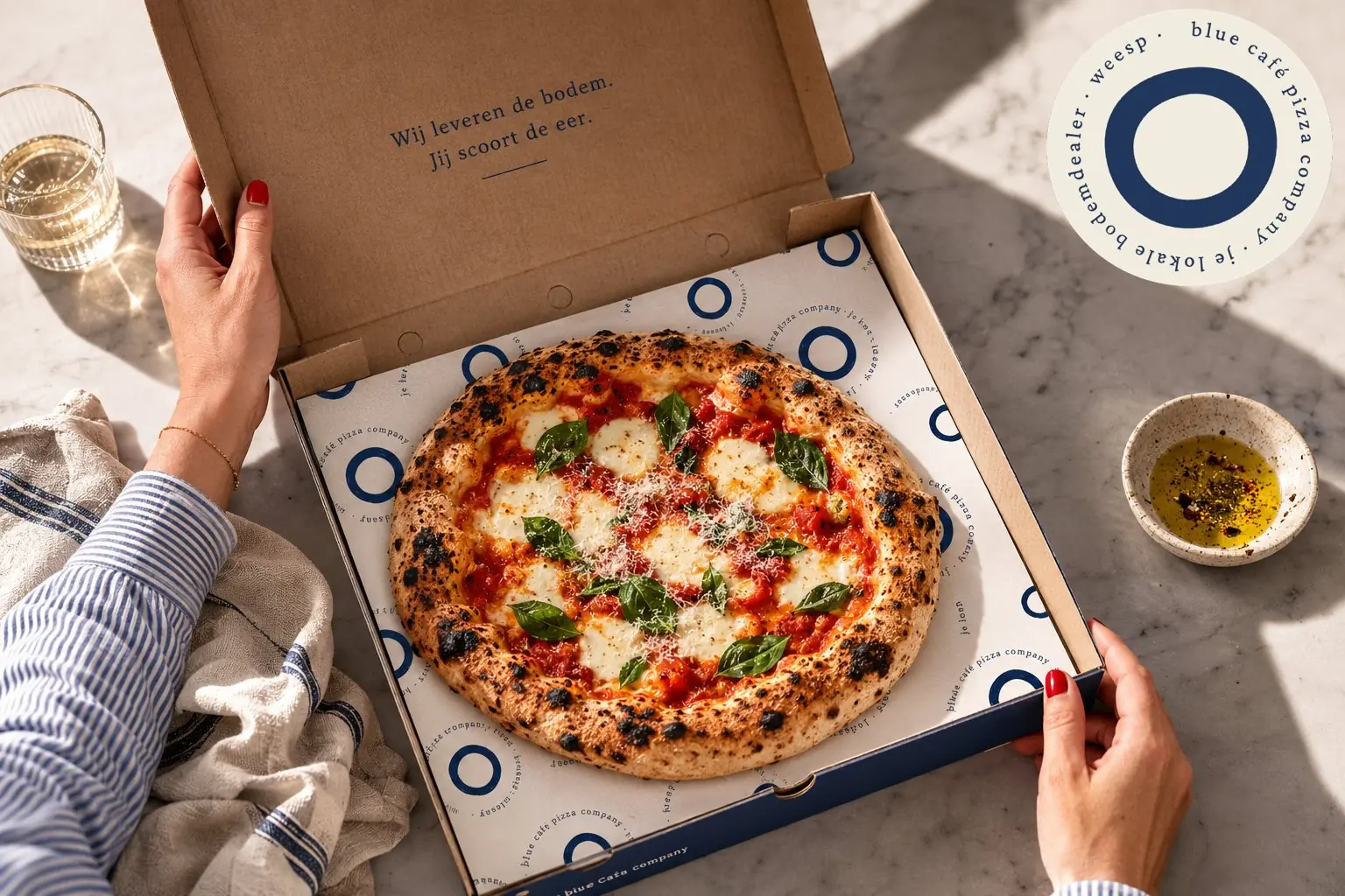 Open Blue Café pizzadoos met verse margherita, quote op de klep: Wij leveren de bodem, jij scoort de eer