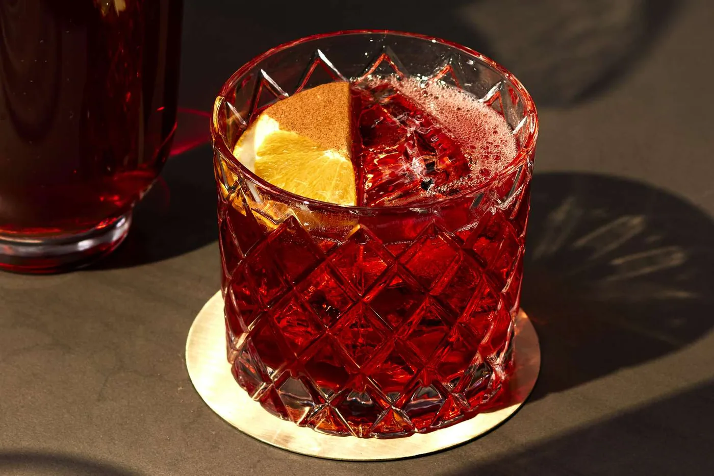 Negroni in een geslepen tumbler met een schijf sinaasappel, in hard middagzonlicht