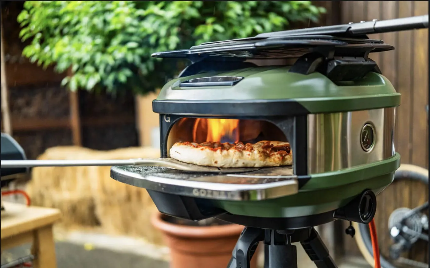 Gas-pizzaoven met vlammen en een verse pizza op de schep, buiten in de tuin